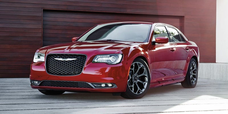 Red Chrysler 300 sedan parked in front of a modern wooden garage door.