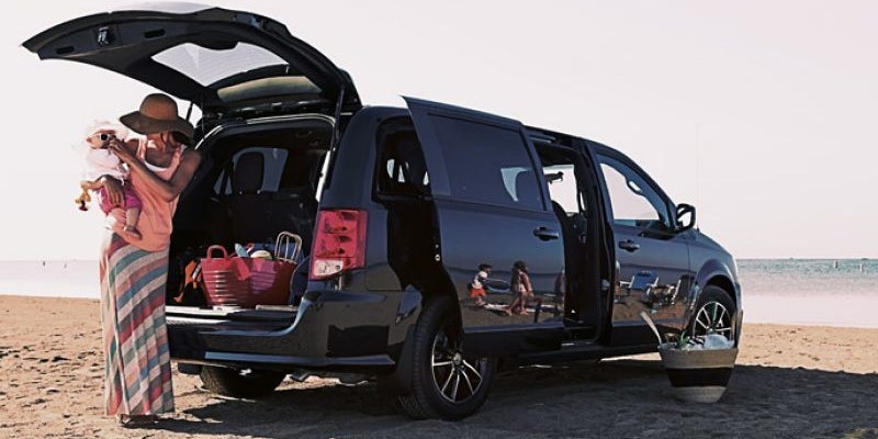 Black minivan parked on a sandy beach with trunk and side doors open. A woman holding a baby stands by the open trunk.