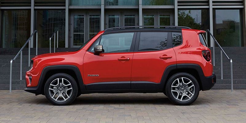 Red Jeep Renegade SUV parked sideways on a paved area in front of a modern building with large windows.
