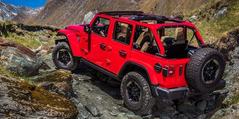 Red Jeep Wrangler Rubicon off-roading on a rocky mountain trail with its top removed and tan seats visible.