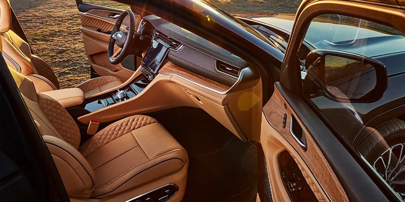 Luxurious tan leather car interior with wood trim, large display screen, and an open driver's side door.
