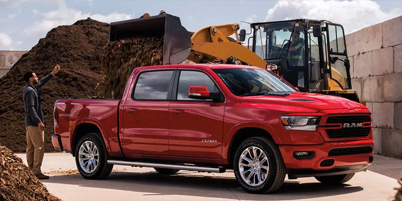 Red Ram pickup truck getting loaded with mulch by a front-end loader, with a man standing nearby.
