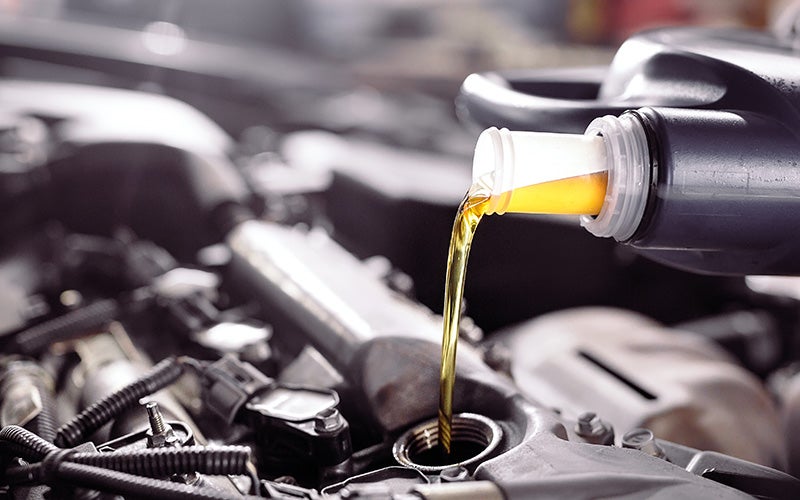 Yellow motor oil pours from a bottle into a car engine's oil cap.
